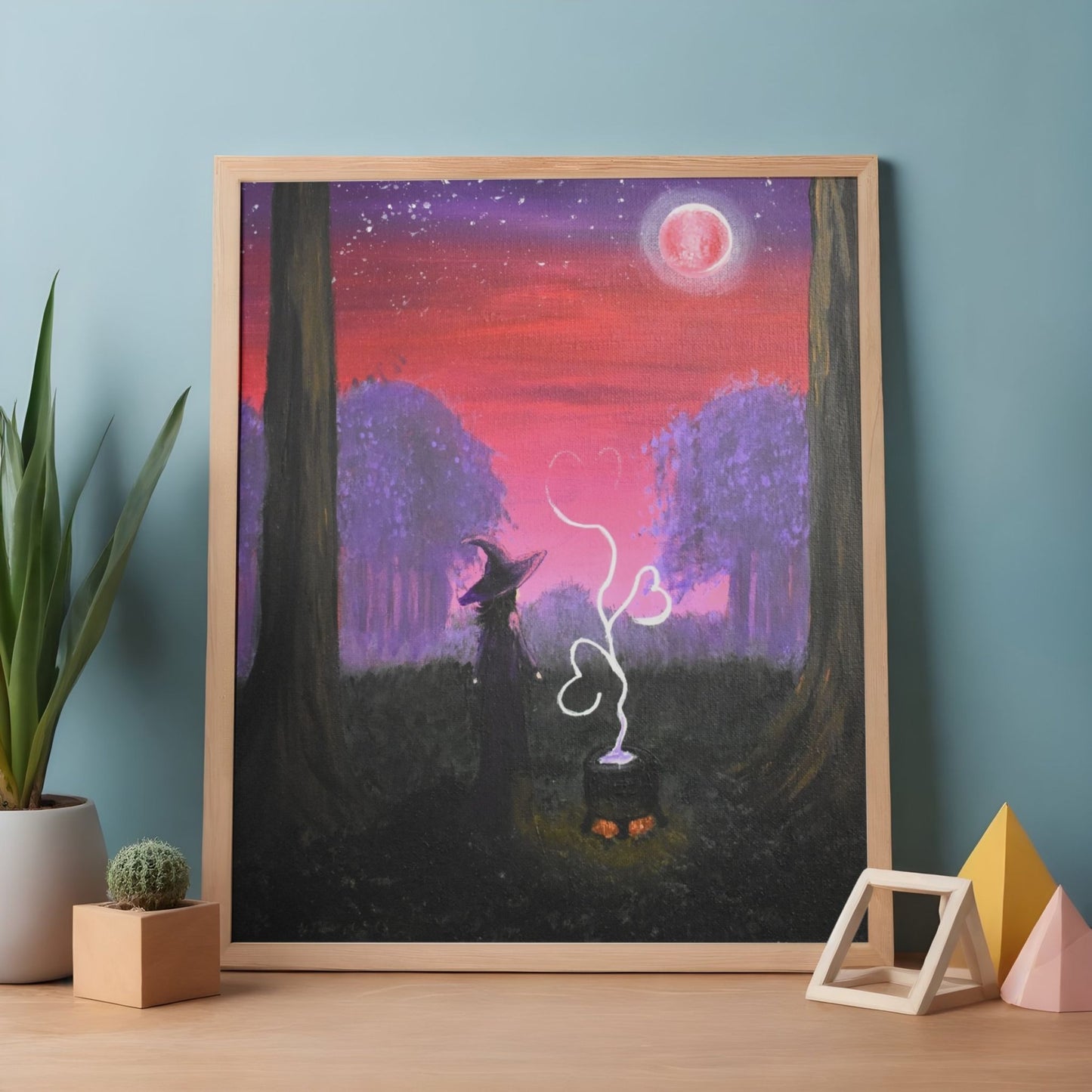 Framed artwork of a fox and rabbit in a forest with a purple sky, on a wooden table.